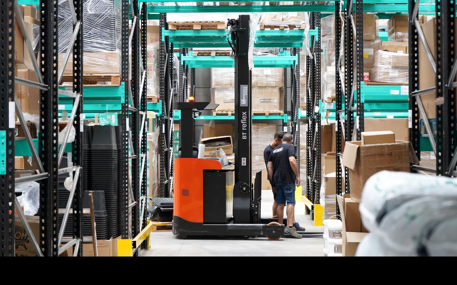 Warehouse workers operating around storage racks and a forklift